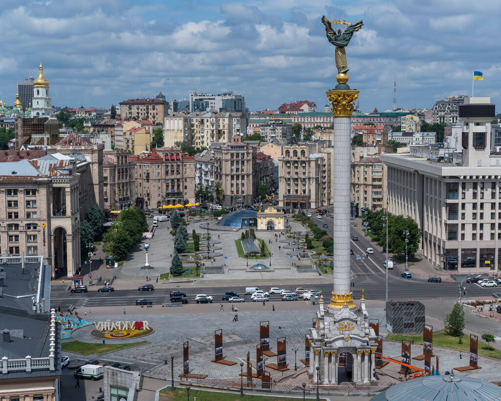 A tall monument stands in the center of Maidan Square in Kyiv, Ukraine, under a blue sky.
