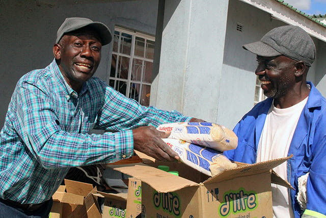 Sinoia Nyamukapa, a teacher at Nyadire High School, hands food to Tobias Gombera, farm supervisor for the school, at Nyadire Mission in Mutoko, Zimbabwe. The Nyadire Connection, a faith-based nonprofit founded by United Methodists, raised money to provide food for hundreds of families at the mission through the end of the year. Photo by Kudzai Chingwe, UM News.