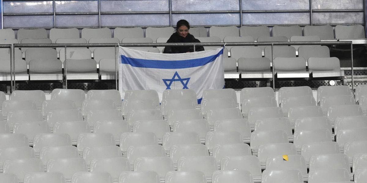 A woman waits next to an Israeli flag before the UEFA Nations League soccer match between France and Israel at the Stade de France stadium in Saint-Denis, outside Paris, Thursday Nov. 14, 2024. (AP Photo/Michel Euler)