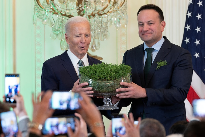 Two men hold up a bowl of shamrocks