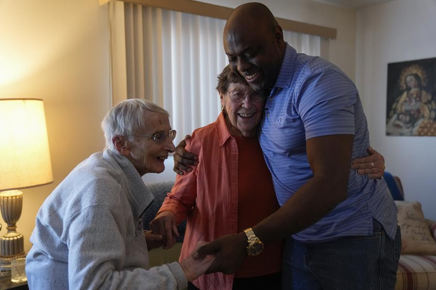 Catholic nuns hug an immigrant man who they work with.