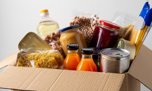 Box with canned food items, pasta, dried beans, juices, and canned fish.