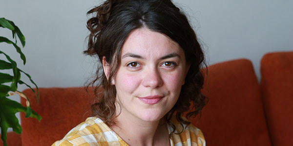A person sitting on an orange couch looking at the camera and smiling