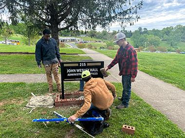 3 male high school students build a brick base for a sign outside