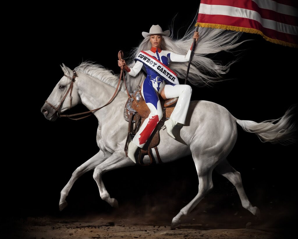 Beyoncé atop a white horse, holding an American flag in her left hand and the reins in her right. She is wearing a red, white and blue rancher’s outfit with a sash reading “Cowboy Carter” across her torso.