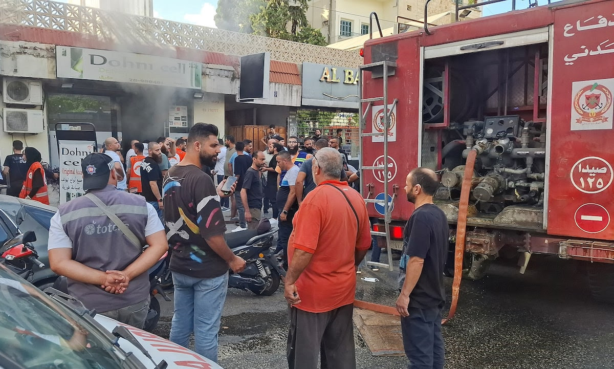 People gather as smoke rises from a mobile shop in Sidon, Lebanon September 18, 2024.