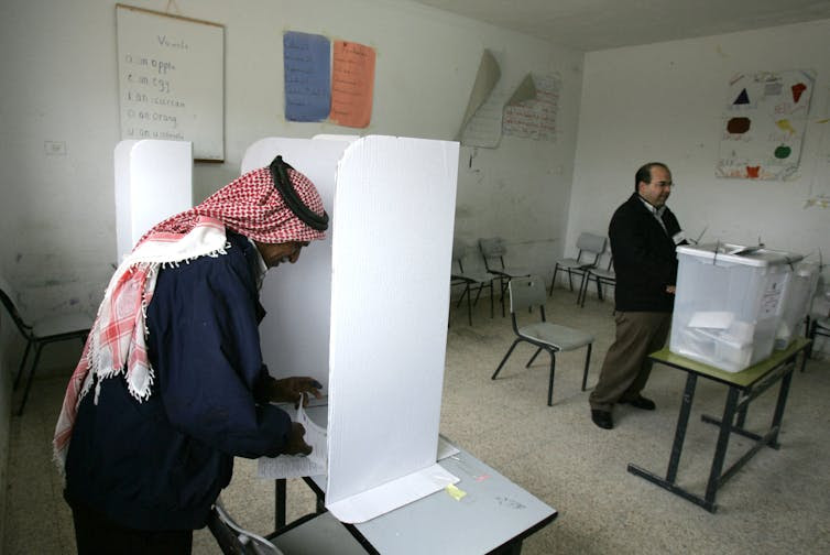 Two men stand at a voting booth in a room