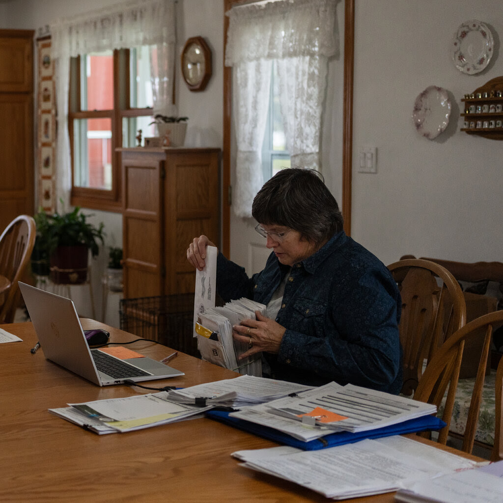 Graceann Toberman, who is sitting at a kitchen table, holds a stack of papers.