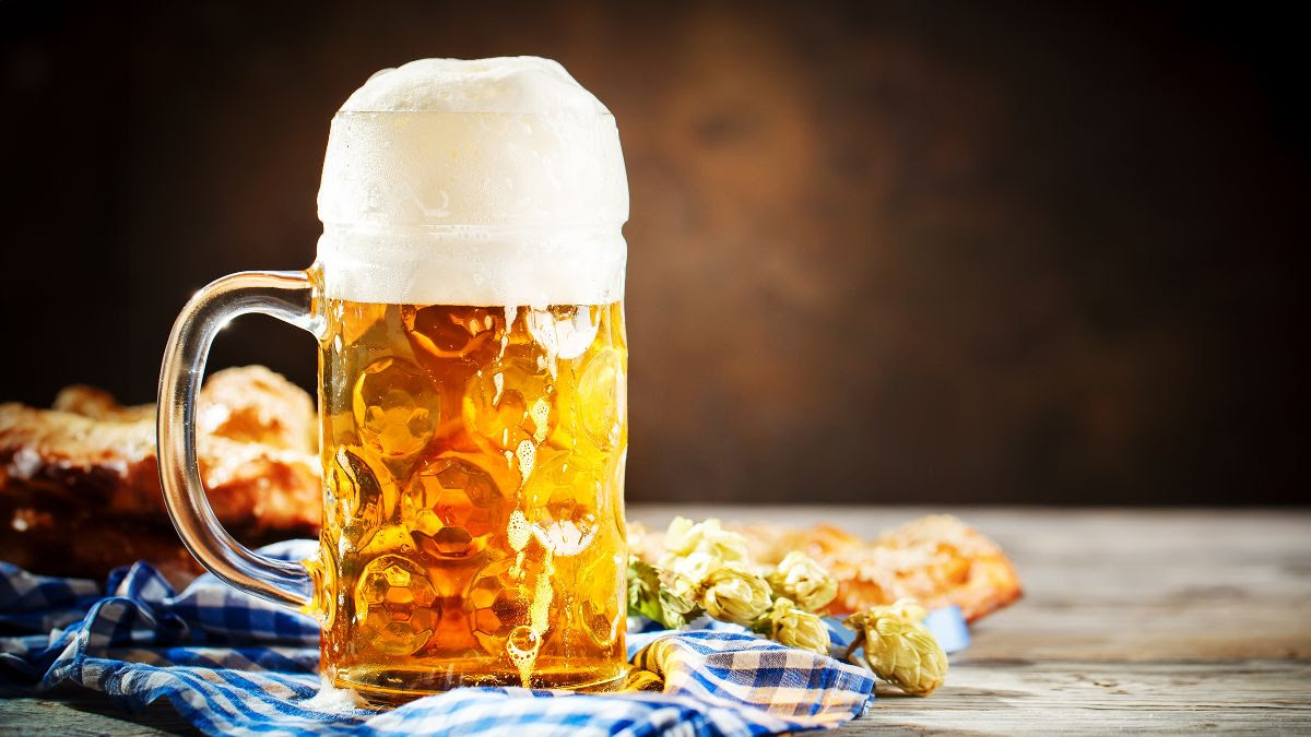 Glass of amber colored beer on a table with fall hops and a blue and white checkered tablecloth