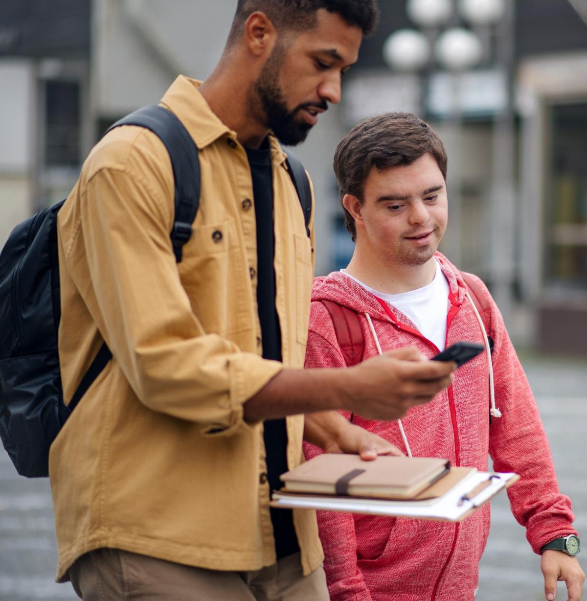 black staff person walking with and showing a cell phone to a white man with Down Syndrome 