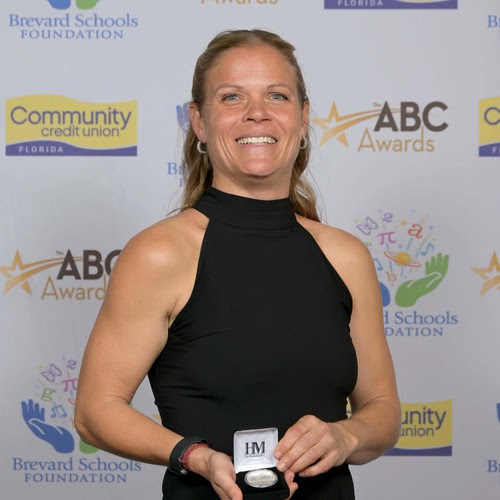 a photo of Laura Negi in front of the awards backdrop smiling and holding her award