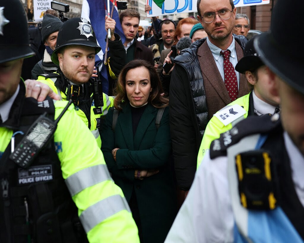 Stella Assange, wife of Julian Assange, leaves court in London, surrounded by supporters and members of law enforcement.