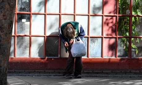 What appears to be a very skinny white man bent over at the waist, on a city street, clutching his hands together. We cannot see his face.