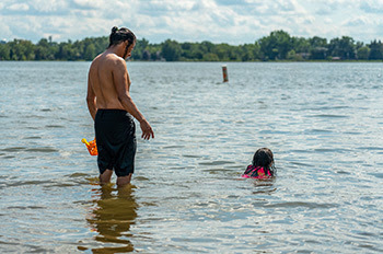 adult watching child playing in water with life jacket