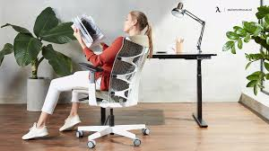 A woman relaxes in a white modern ergonomic office chair, leaning back comfortably as she reads a book. The setting is bright and contemporary, emphasizing a sense of calm and focus."