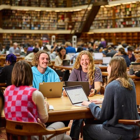 Students sit at a table in a Library smiling.
