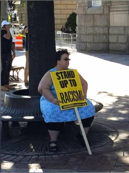 A person seated with sign that says stand up against racism.