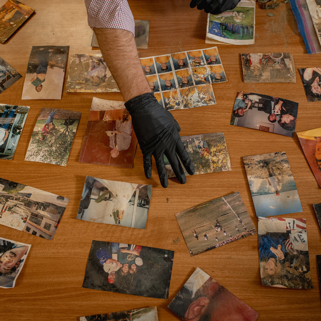 A man wearing latex gloves touches a photo that is among many laid out on a table.