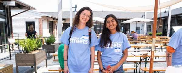 two volunteers at tour de streets smile at the camera while wearing light blue tour de streets t shirts