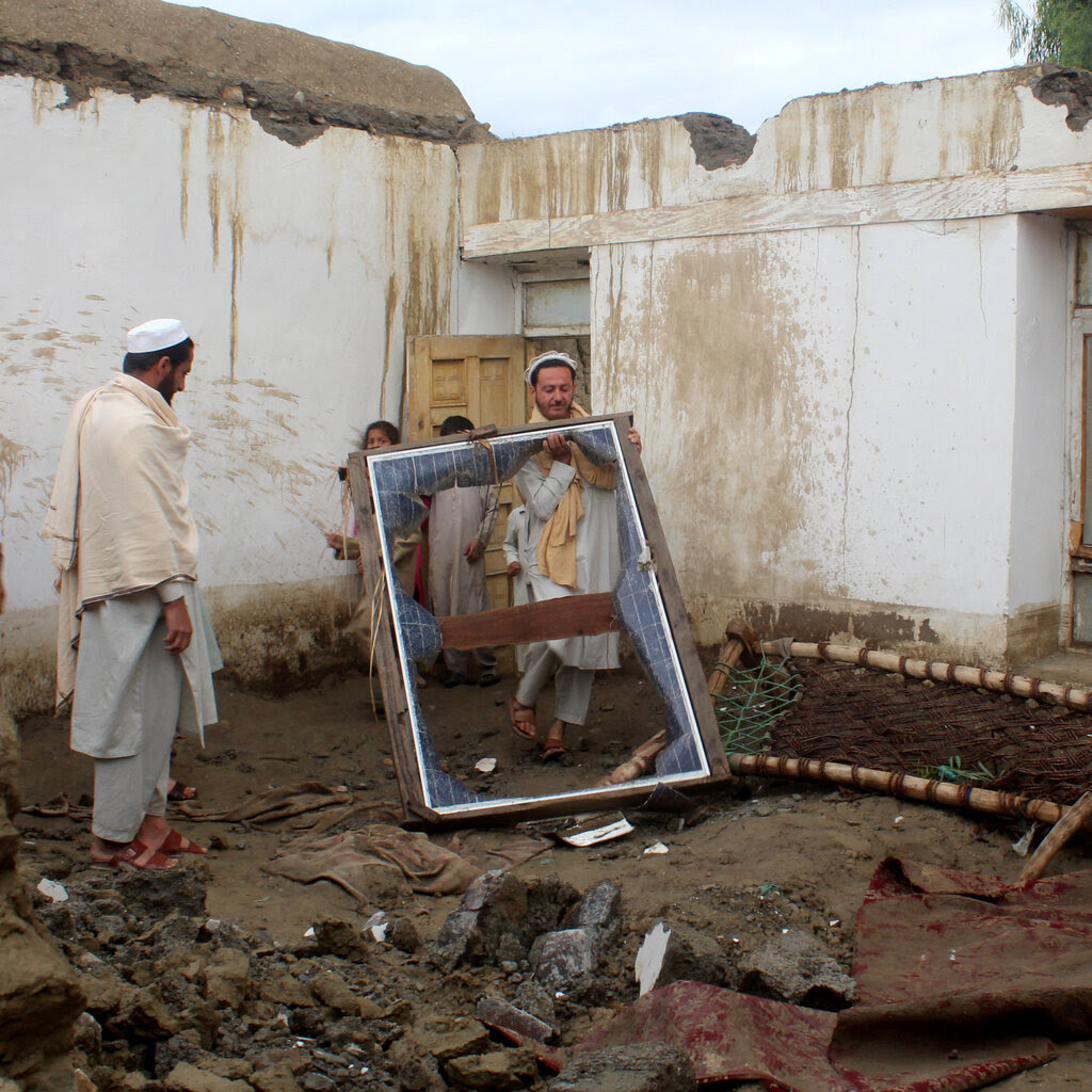 Figures carrying damaged items in a muddy courtyard.