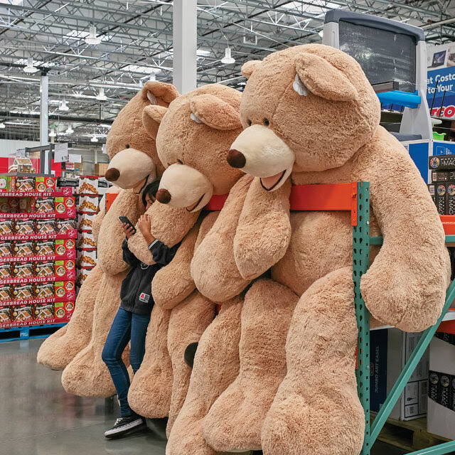 A girl stands with one hand wrapped around a gigantic stuffed bear and the other holding her phone. 