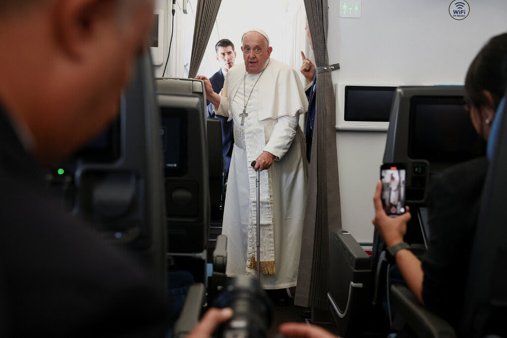 Pope Francis in the aisle of an airplane.