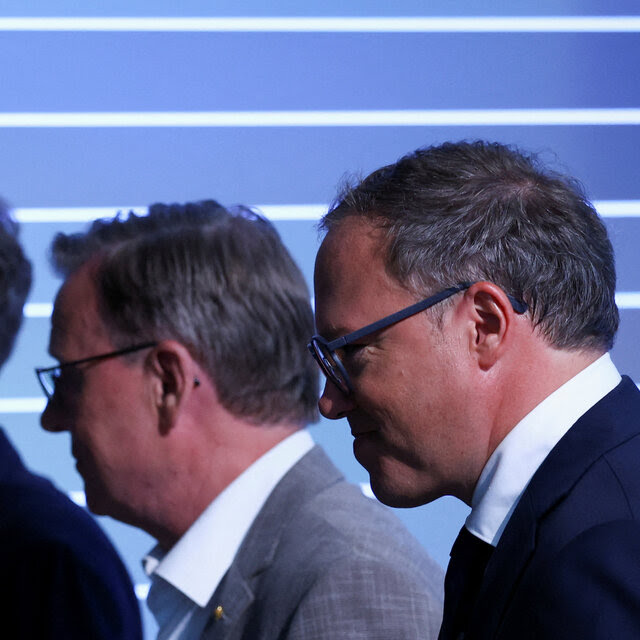 Three men in suits, two wearing glasses.