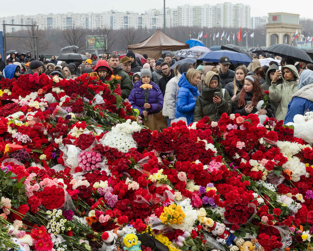 Crowds standing in front of piles of flowers.