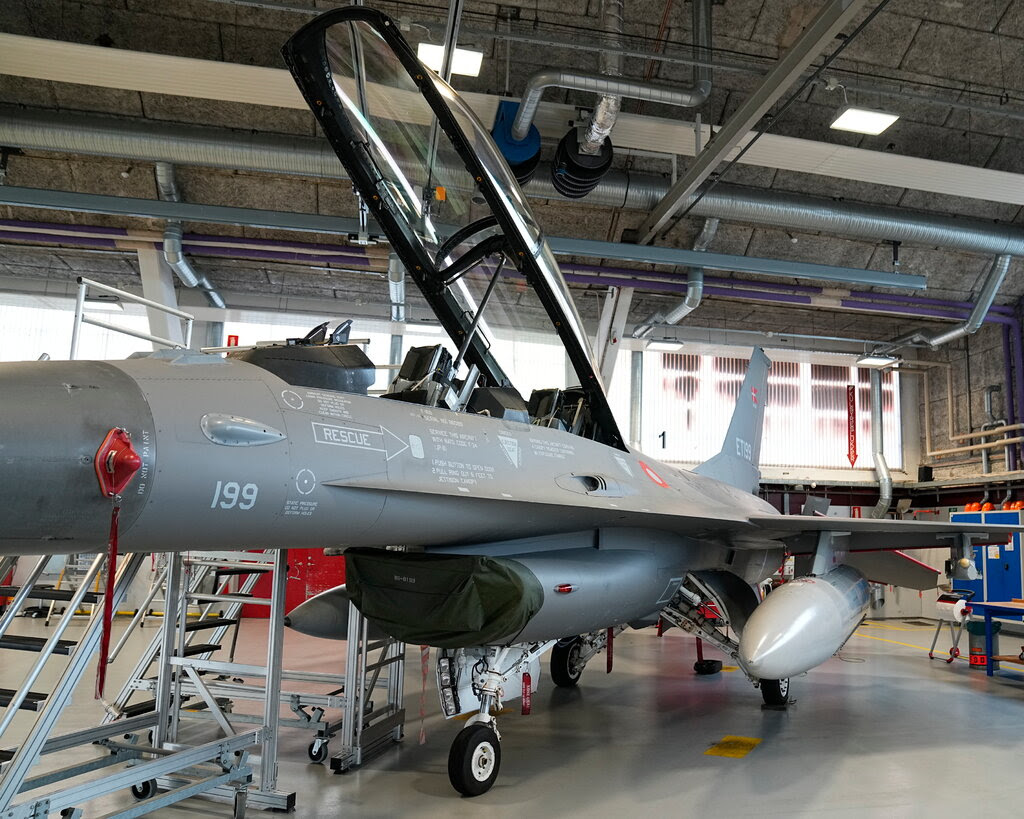 An F-16 jet sits inside a building with its cockpit canopy open.