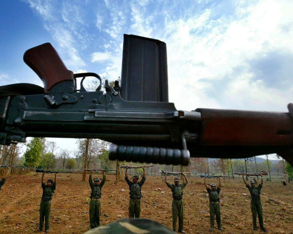 A rifle is held upside in the foreground, while in the background, several rebels hold rifles over their heads.