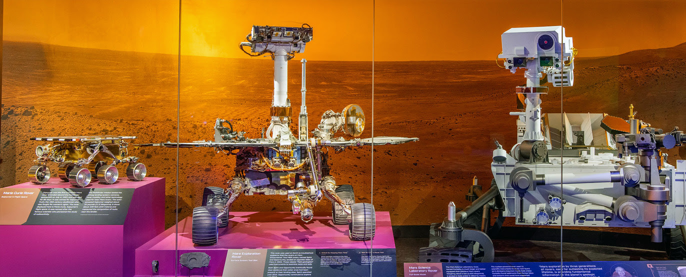 Three rovers, each about twice the size of the other (left to right) are on display in a museum exhibition.