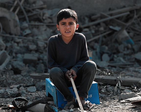 A photo of a boy sitting in the middle of ruins