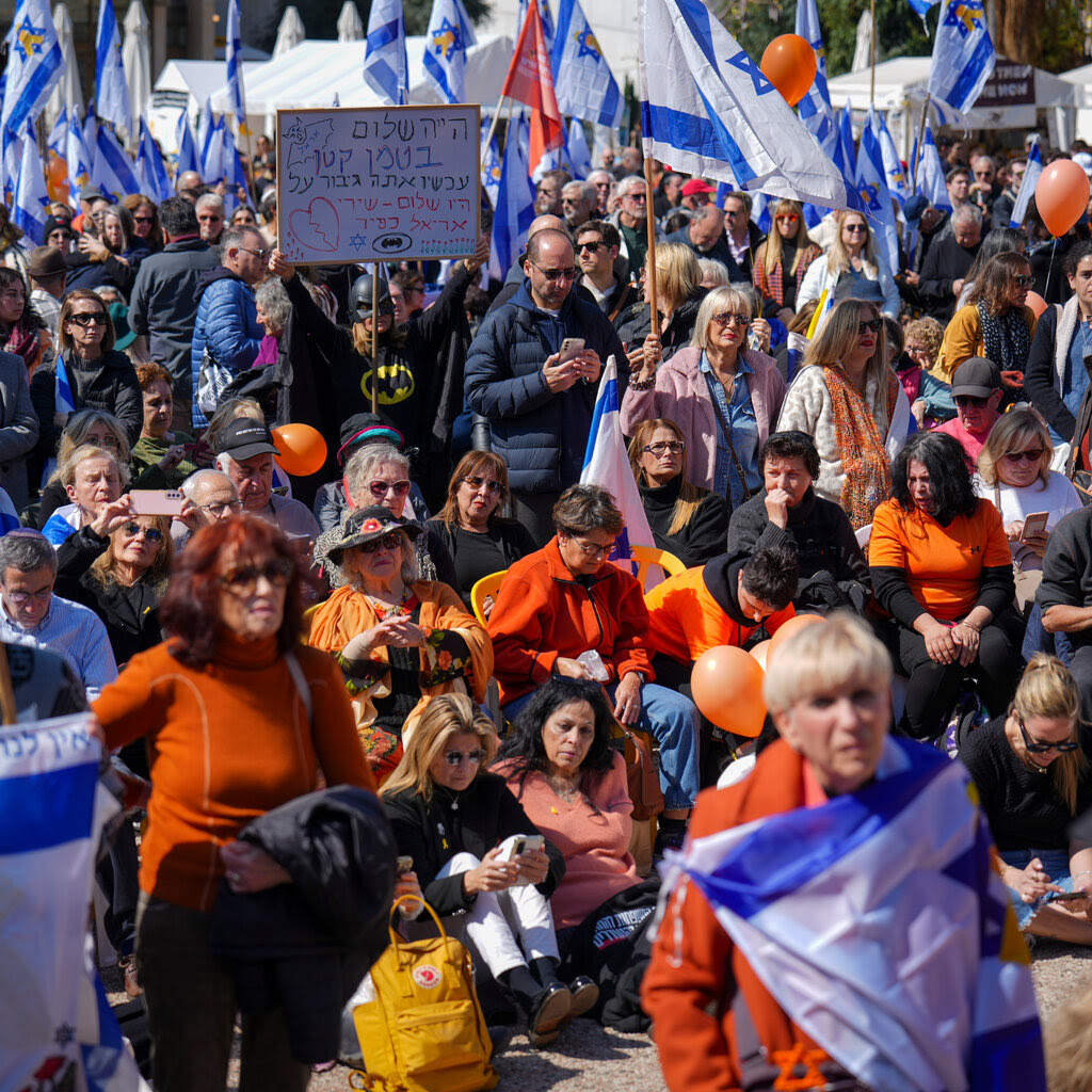 A crowd of people, many wearing orange and carrying Israeli flags.