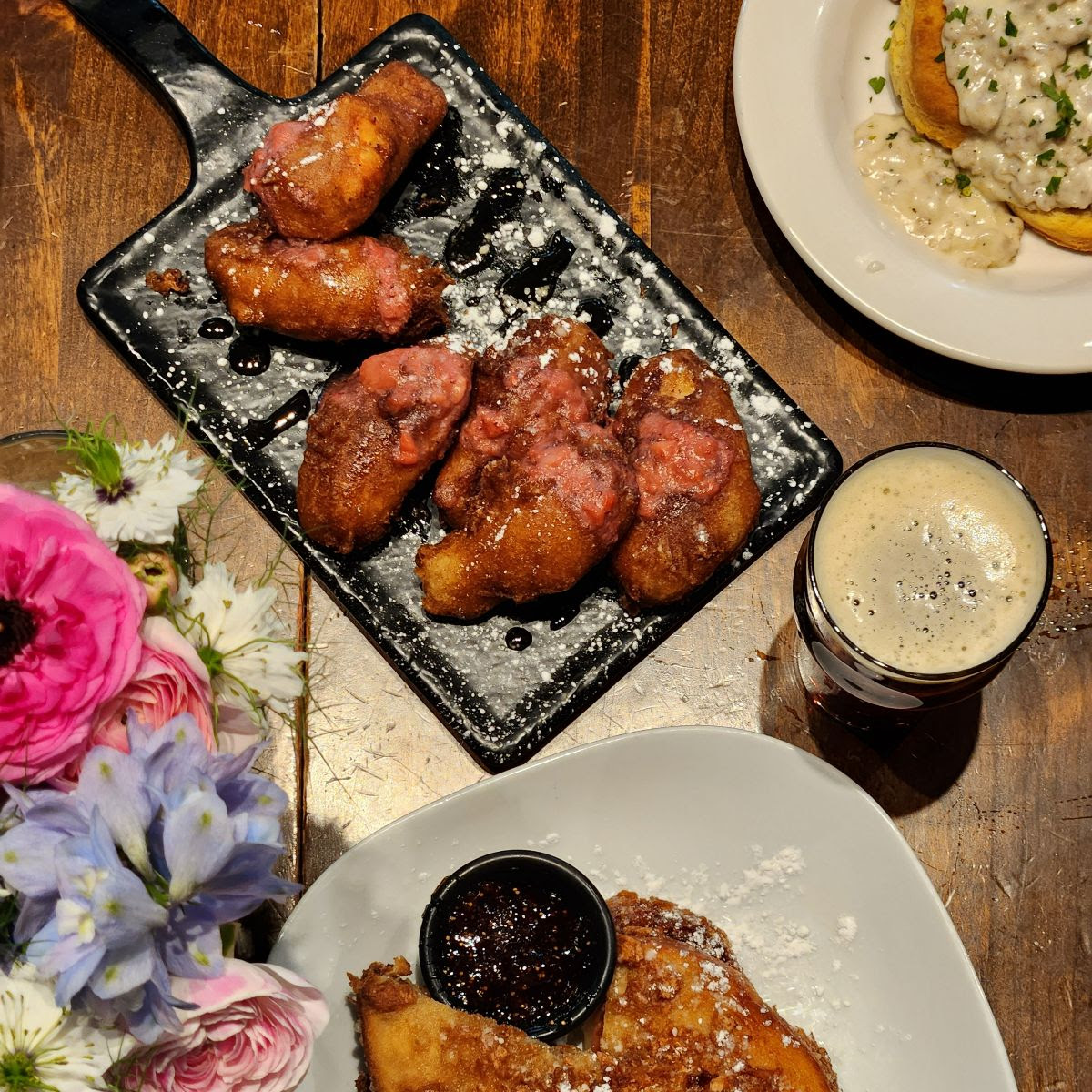 Aerial shot of various items from the GLBC brewpub brunch menu, with a pint of beer and a floral centerpiece.