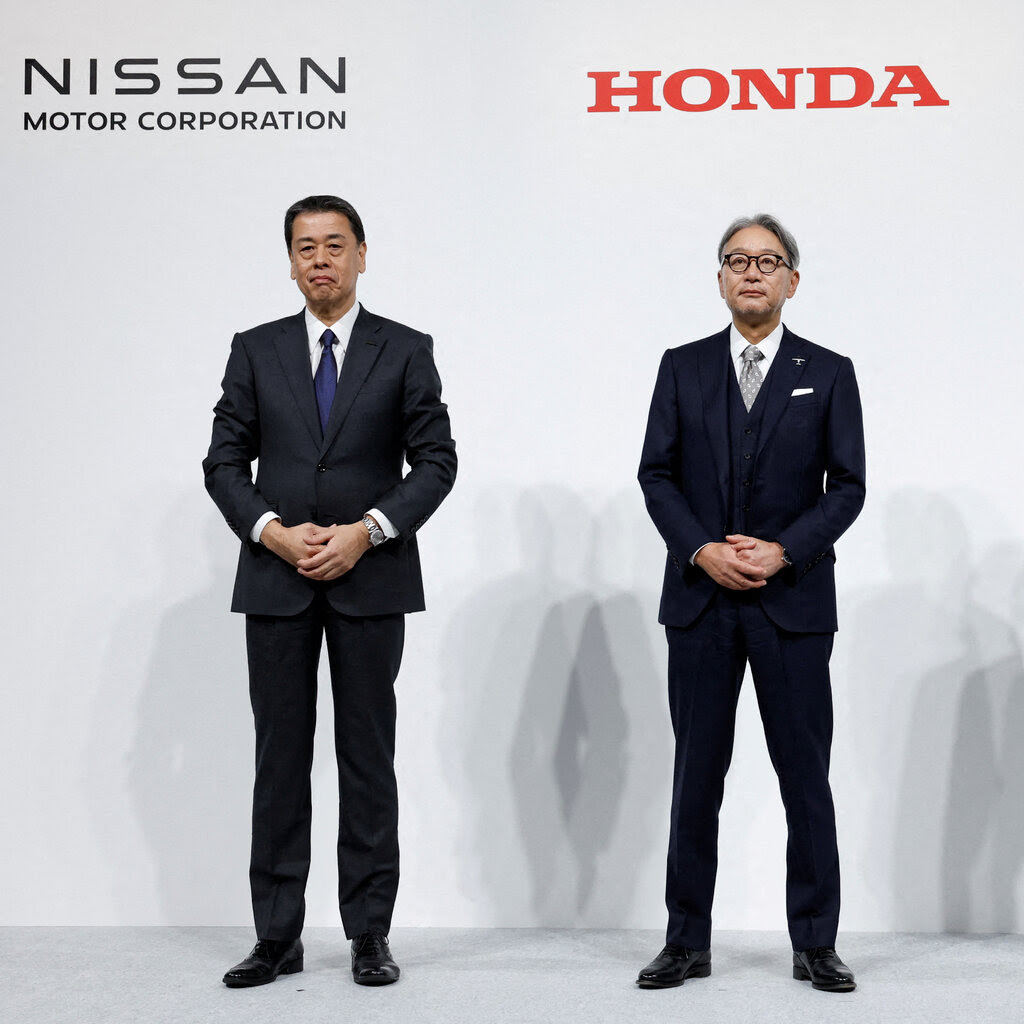 Two men in suits standing under labels that read “Nissan Motor Corporation” and “Honda.”