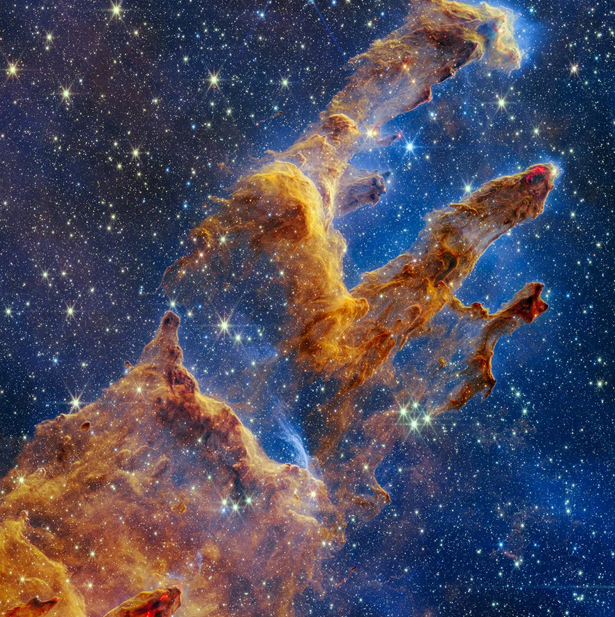 Photo of the Pillars of Creation in orange dust on a deep blue background of starry space