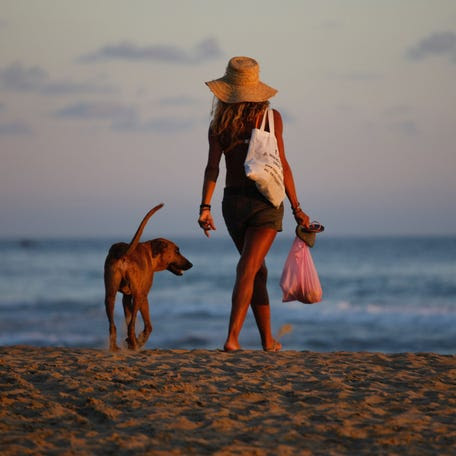 A woman walks with her dog on the beach as the sun sets behind the Pacific Ocean in Zipolite, Oaxaca state, Mexico on Dec. 14, 2017.