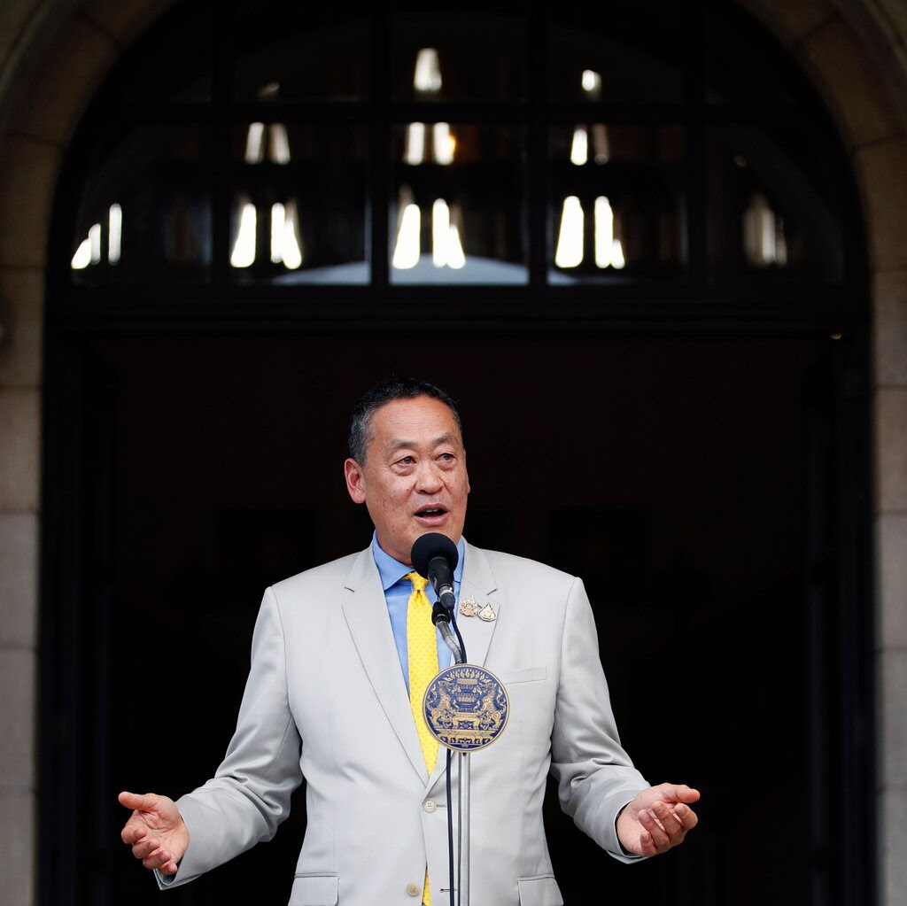 Srettha Thavisin speaks into a microphone while standing in front of an arched, stone entryway to a building.