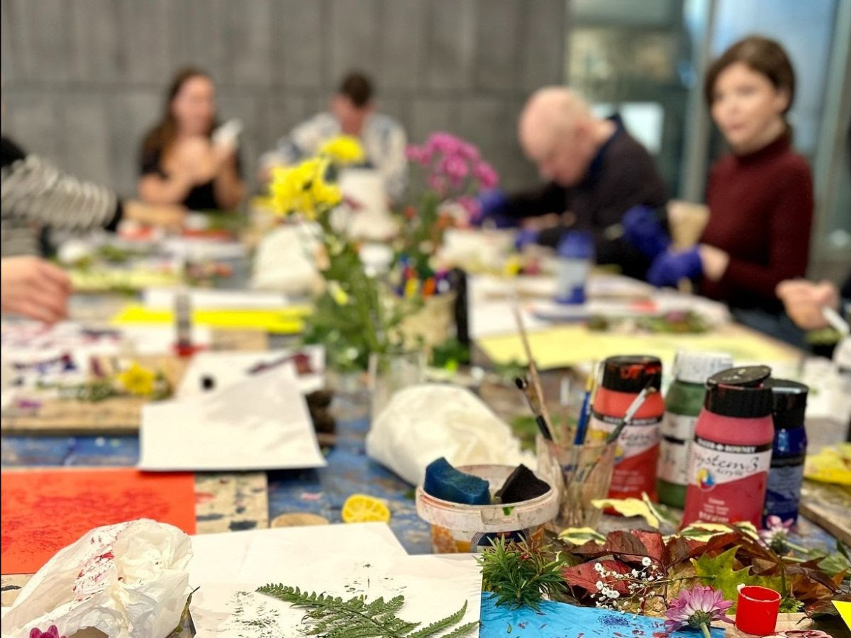 Art and Wellbeing Class with plants and paint on a table and a group of adults working away.