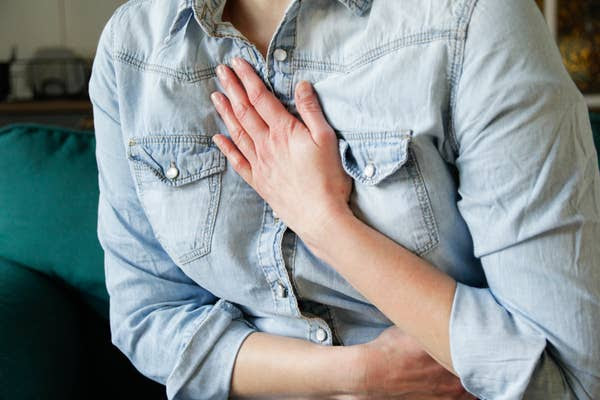 Person in a denim shirt holds their chest with one hand and their stomach with the other, appearing to be in discomfort