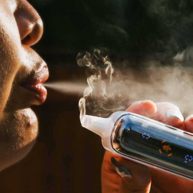 A woman holds a vape while blowing smoke out of her mouth.