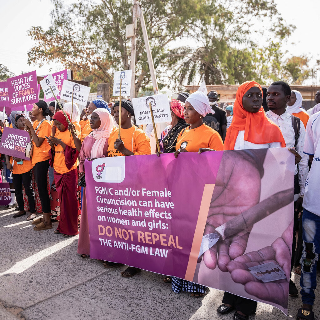 Men and women in Gambia holding posters and signs asking legislators not to repeal the law banning female genital cutting.
