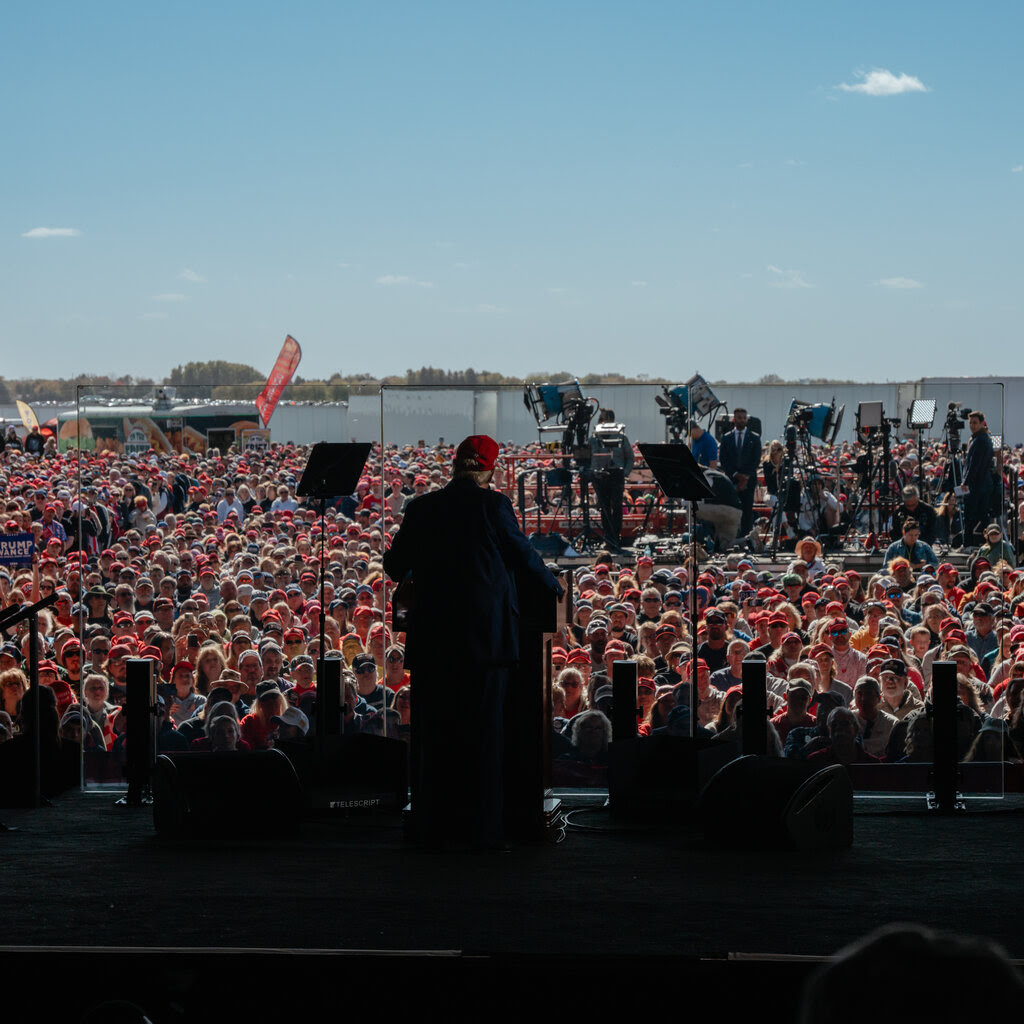 Donald Trump, shown from behind, standing and speaking to a crowd.