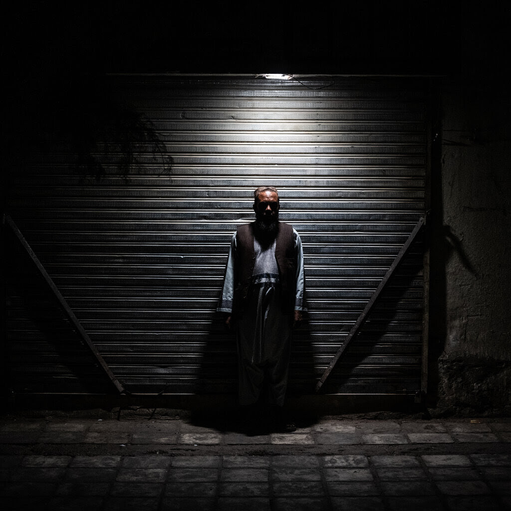 An Afghan man stands in the shadows against a metal door.