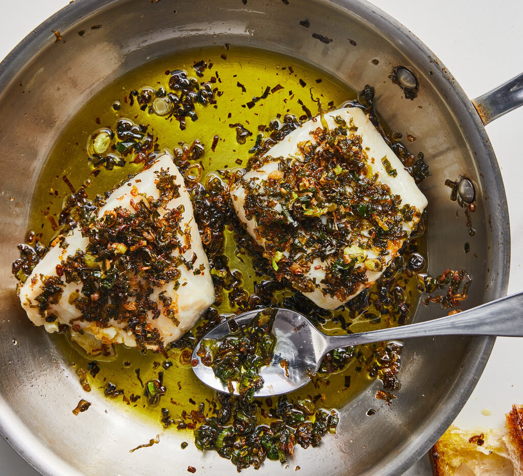 Two white fish fillets in oil and topped with fried onions. 