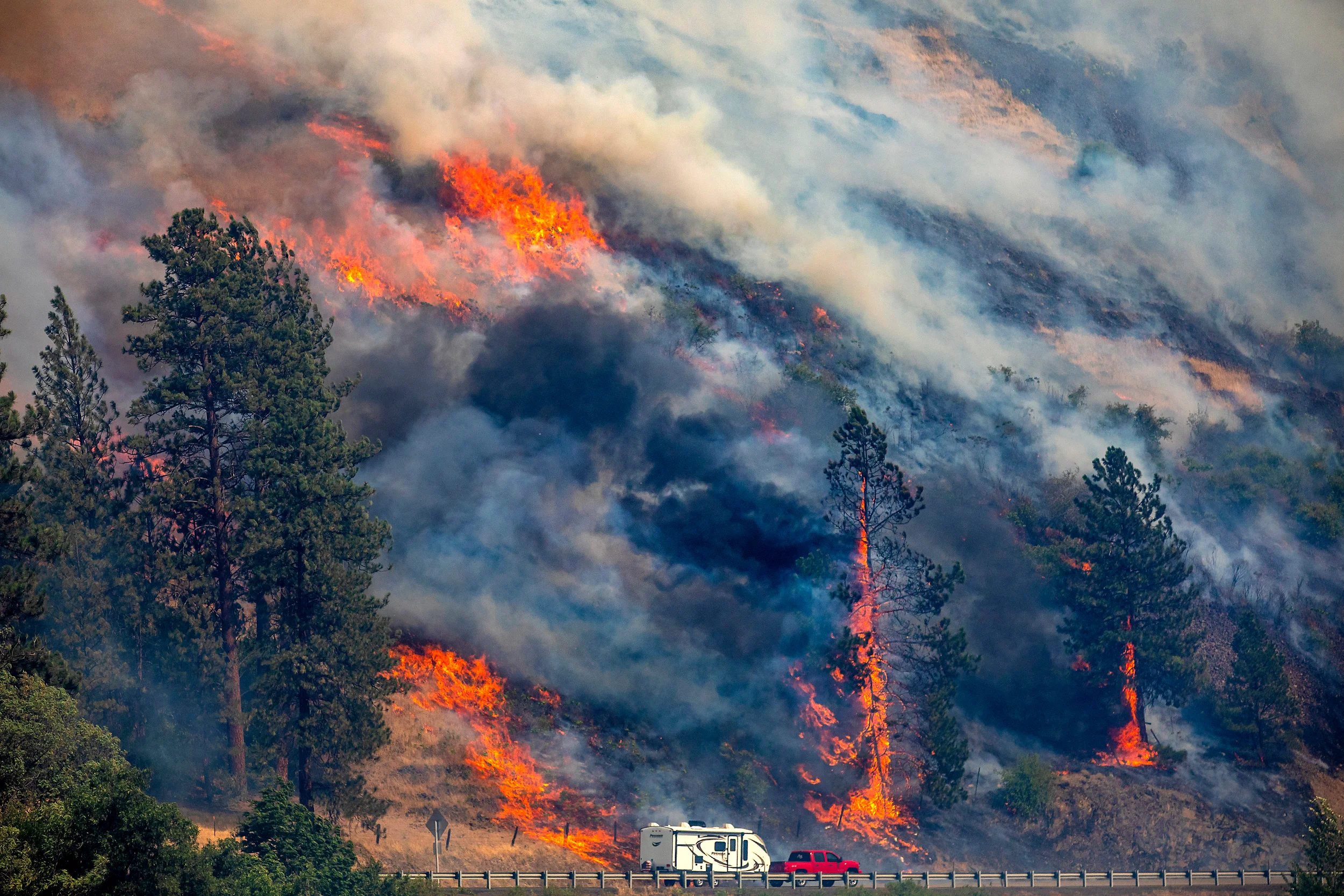 A vehicle drives past the spreading River Fire Thursday, July 25, 2024, near Myrtle, Idaho, before U.S. Highway 12 was closed. Lightning strikes have sparked fast-moving wildfires in Idaho, prompting the evacuation of multiple communities. (August Frank/Lewiston Tribune via AP)