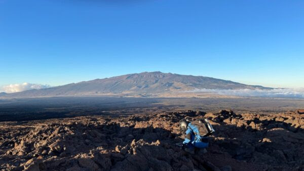 A woman in a space suit near a volcano.