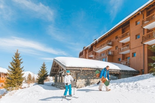 A person and person with skis and snowboards in front of a buildingDescription automatically generated