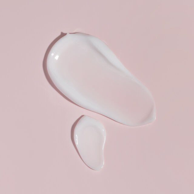 Two lotion smears on a pink backdrop.