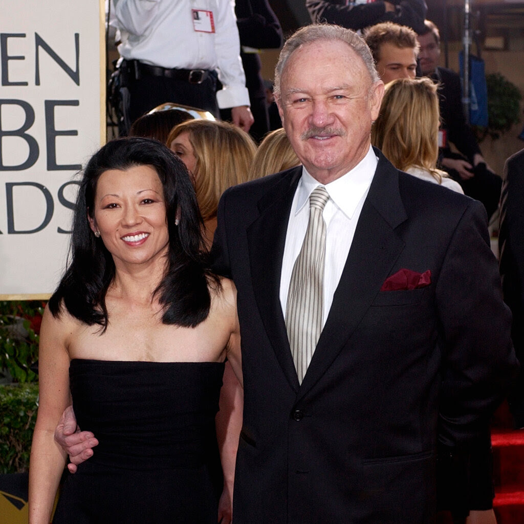 Gene Hackman in a suit with a cream-and-black striped tie, and Betsy Arakawa in a black strapless dress.